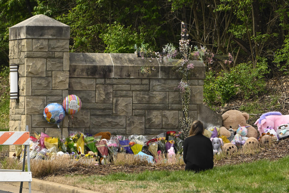 A person kneels in front of an entry to Covenant School which has become a memorial for shooting victims, Tuesday, March 28, 2023, in Nashville, Tenn. (AP Photo/John Amis)