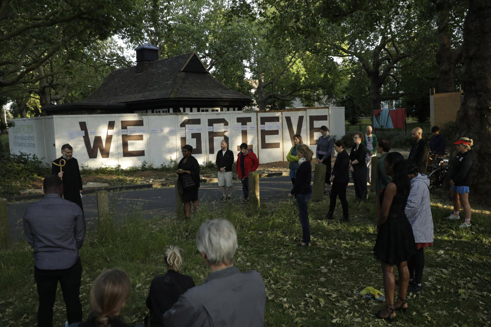 Reverend William Taylor, top left, and local people standing with social distancing observe a 30 second silence during a remembrance event as they add the names of five people who recently died to the community "We Grieve" wall at Clapton Common, in London, Thursday, May 28, 2020. The "WE GRIEVE″ wall has become a focal point for people who gather Thursdays to remember those who have died during the coronavirus pandemic, and organizer Rev. William Taylor says that the community found that there was a need just to stand together to grieve.(AP Photo/Matt Dunham)