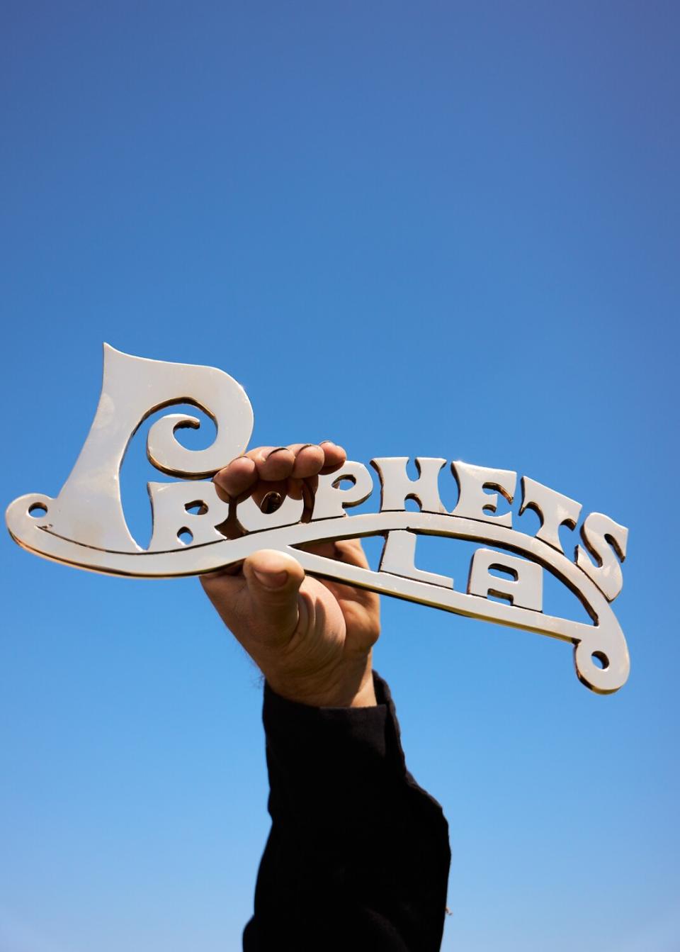 "Prophets LA" lowrider plaque designed by Pinche Kid held up to the sky by plaque maker David Lopez