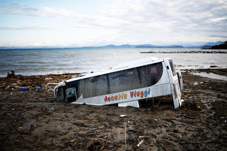 A white bus sinking into mud; behind it is a blue coastline