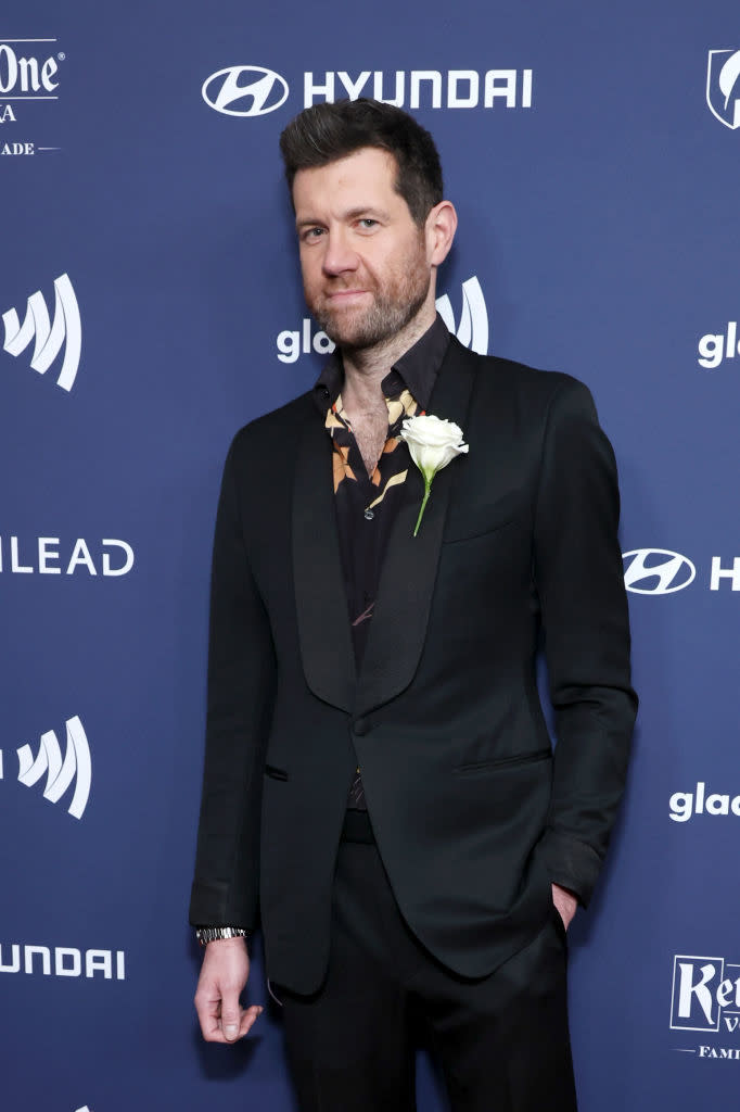 Billy Eichner in a suit with a corsage, posing on the red carpet