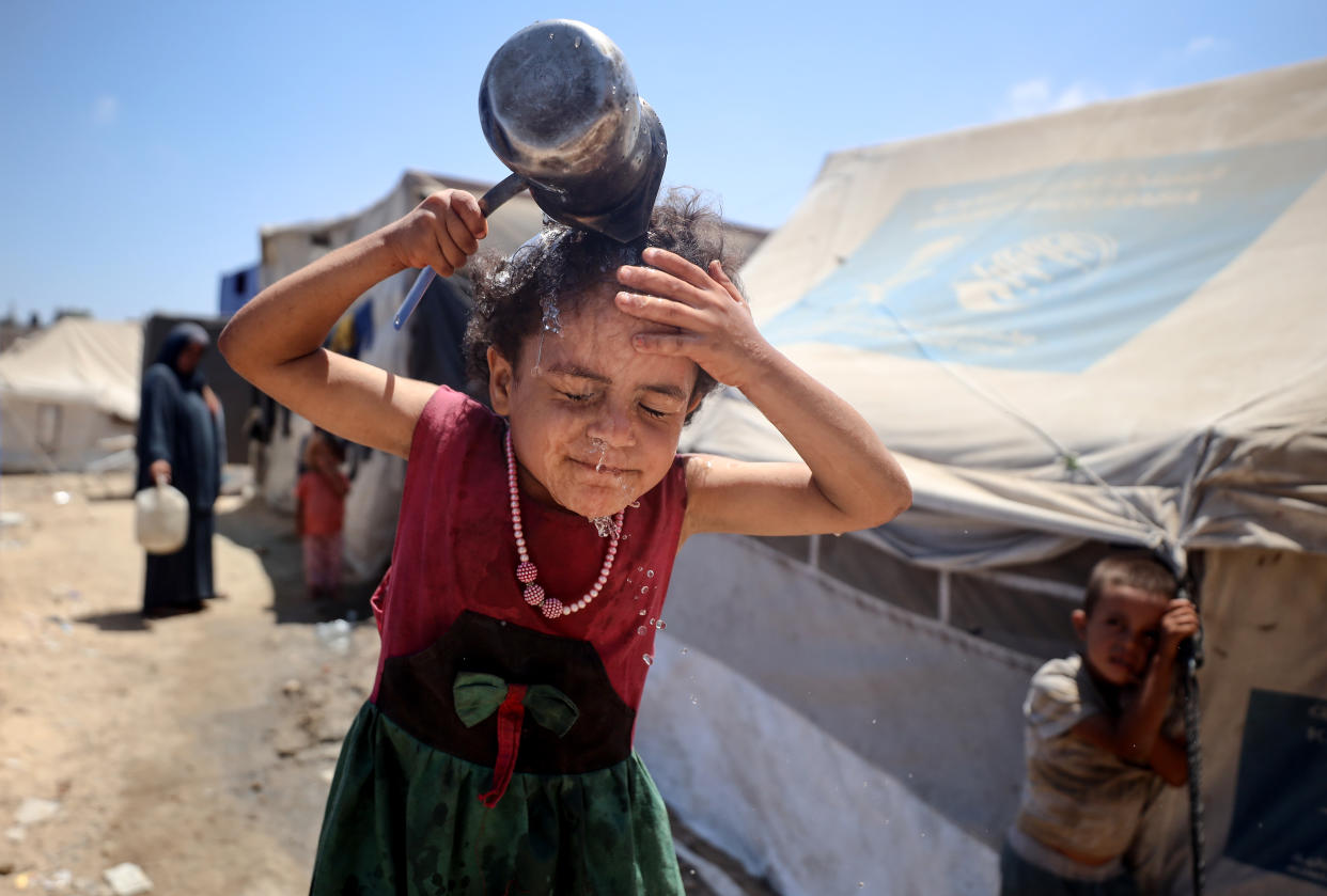 A young girl pours a container of water over her head.