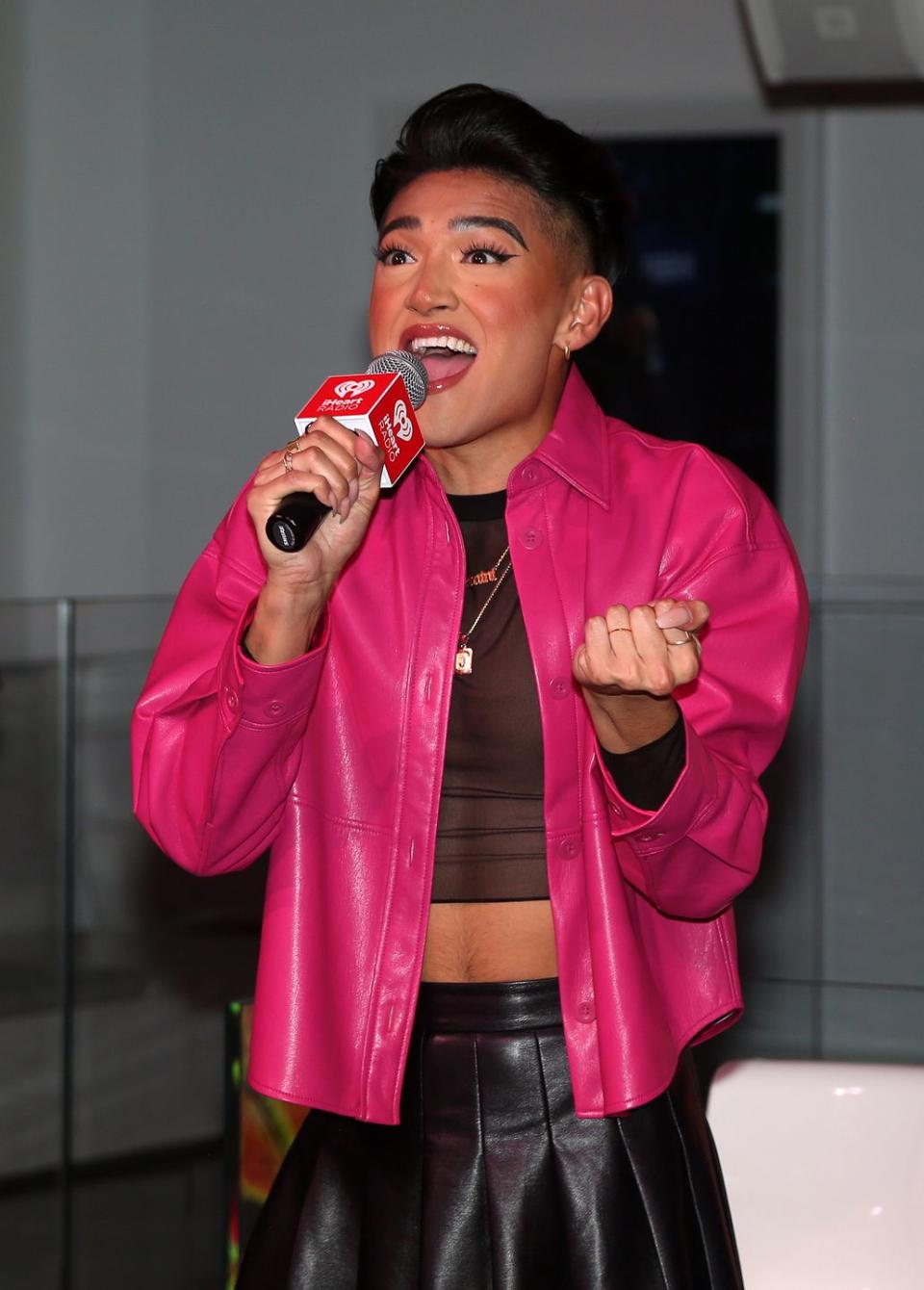 justin david sullivan, wearing a pink coat and black top, sings into a microphone
