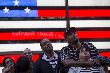 People stand in front of a billboard by Revlon that takes their pictures and displays them on the billboard in Times Square in the Manhattan borough of New York October 13, 2015. REUTERS/Carlo Allegri