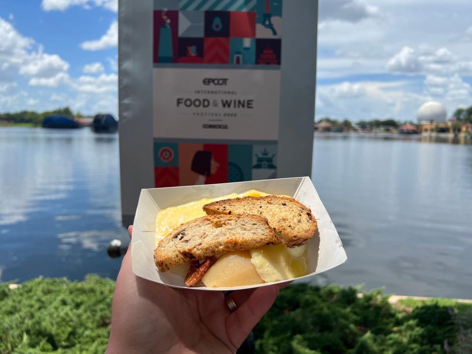 hand holding carton of food from epcot food and wine festival in front of the lagoon