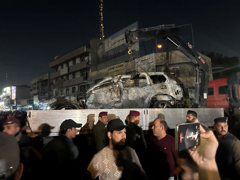 People gather as a destroyed vehicle is loaded onto a truck, after a deadly drone strike in Baghdad