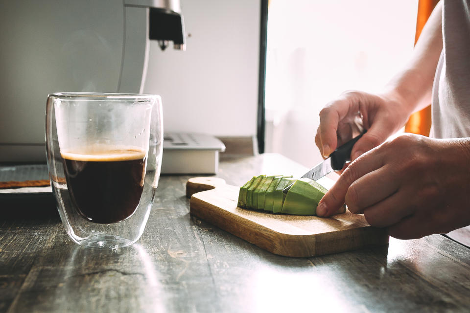 Cutting avocado on a wooden cutting board with coffee cup