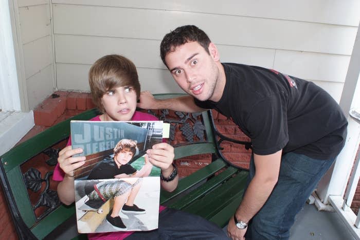 Scooter Braun leaning down towards a younger Justin Bieber who's holding a poster of himself