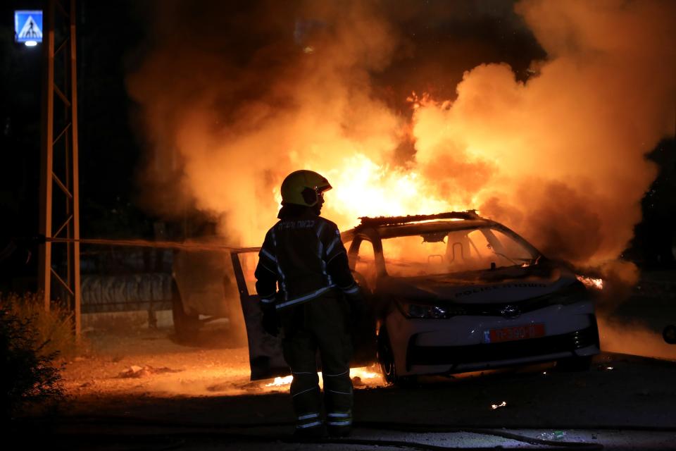 <p>An Israeli firefighter by a burning police car in Lod</p> (Reuters)