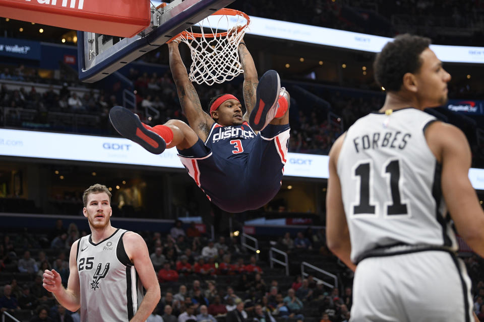 Washington Wizards guard Bradley Beal (3) hangs from the rim after his dunk between San Antonio Spurs center Jakob Poeltl (25) and guard Bryn Forbes (11) during the first half of an NBA basketball game Wednesday, Nov. 20, 2019, in Washington. (AP Photo/Nick Wass)