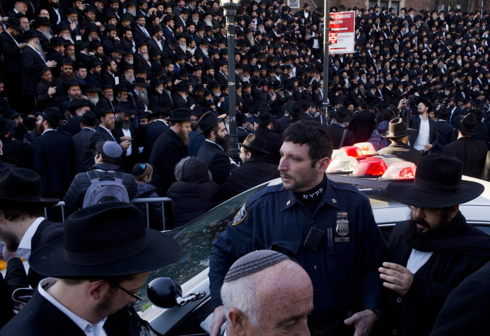 In this Sunday, Nov. 4, 2018, photo a New York City police officer stands next to his patrol car as he watches over crowds of rabbis gathering for a group photo at the Chabad-Lubavitch World Headquarters in New York. More than 5,000 of the orthodox Jewish leaders from around the world are taking part in the annual meeting. The NYPD has increased patrols at houses of worship in light of the recent fatal shooting at a synagogue in Pittsburgh. (AP Photo/Mark Lennihan)