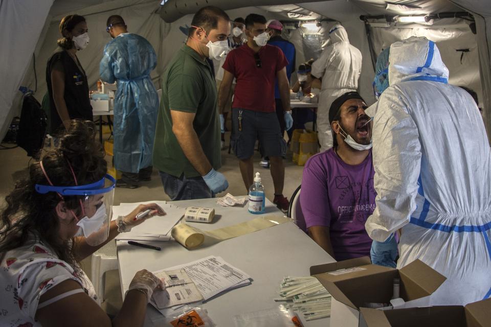 FILE - Medical staff of the National Health Organization (EODY) conduct tests for the new coronavirus from migrants in Moria refugee camp on the northeastern Aegean island of Lesbos, Greece, on Friday, Sept. 4, 2020. A major testing and contact-tracing operation at Greece's largest migrant camp on the eastern island of Lesbos has so far detected 17 confirmed cases of COVID-19 infection among the 12,500 people living in the overcrowded facility, officials said on Tuesday, Sept. 8, 2020. (AP Photo/Panagiotis Balaskas, File)