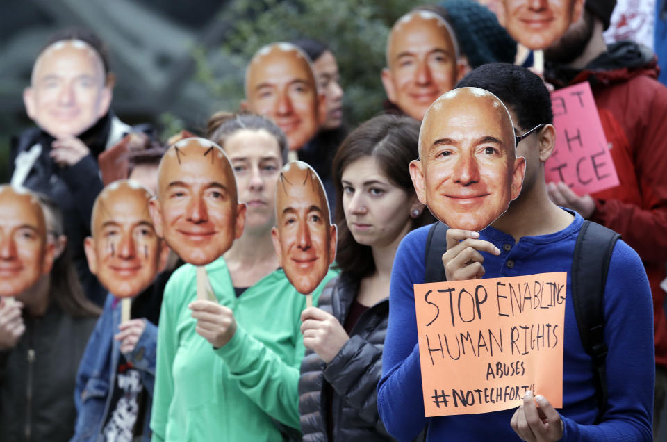 Demonstrators hold images of Amazon CEO Jeff Bezos near their faces during a Halloween-themed protest at Amazon headquarters over the company's facial recognition system, "Rekognition," Wednesday, Oct. 31, 2018, in Seattle. Protesters said that they were there in support of hundreds of Amazon employees who have signed a letter asking the company to stop marketing their facial recognition software to ICE and to drop its contract with software company Palantir and to law enforcement agencies. (AP Photo/Elaine Thompson)