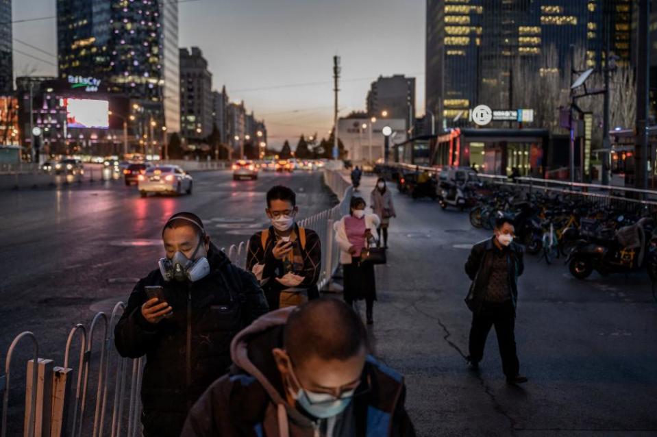 Chinese commuters wear protective masks as they line up in a staggered formation while waiting for a bus at the end of the work day on March 20, 2020 in Beijing, China.