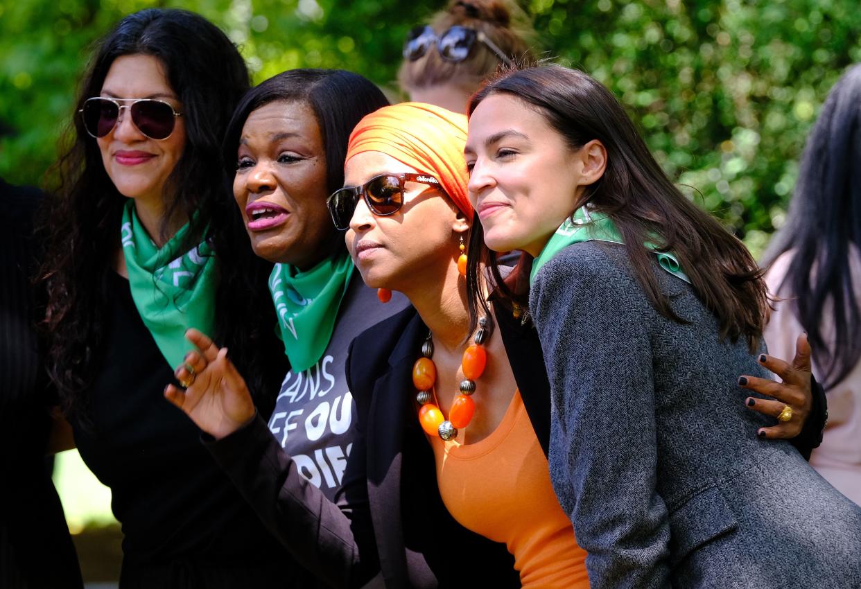 Reps. Rashida Tlaib, Cori Bush, Ilhan Omar and Alexandria Ocasio-Cortez pose for the camera against a green background.