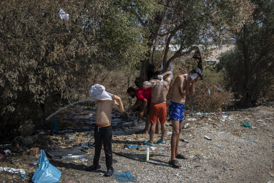 Migrants and refugees wash in a field near the burned Moria camp on island of Lesbos, Greece, Sunday Sept. 13, 2020. Greek authorities have been scrambling to find a way to house more than 12,000 people left in need of emergency shelter on the island after the fires deliberately set on Tuesday and Wednesday night gutted the Moria refugee camp. (AP Photo/Petros Giannakouris)