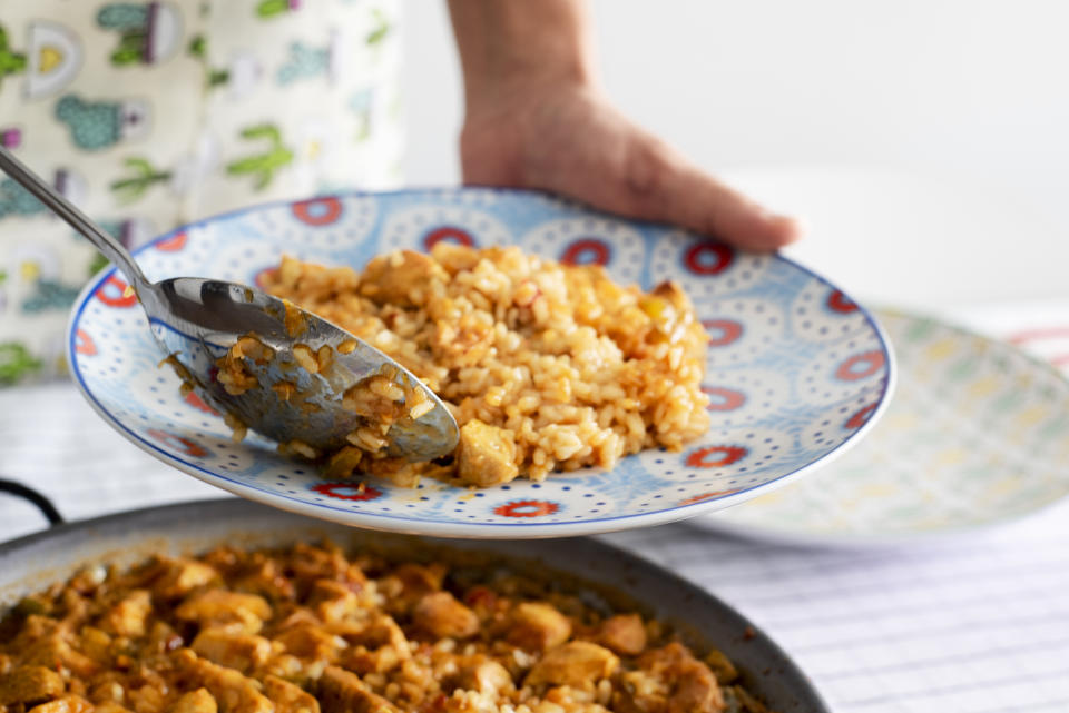 closeup of a young caucasian man serving a plate of spanish chicken paella, from the paellera, the paella pan, freshly cooked