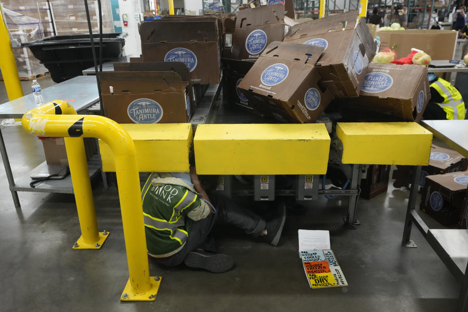 A worker practices "drop, cover, and hold on" under a conveyor belt as boxes fall during a ShakeOut earthquake drill at the Los Angeles Regional Food Bank in Los Angeles Thursday, Oct. 19, 2023. Up and down the West Coast, the ShakeOut drill was scheduled to begin at 10:19 a.m. PDT with a cellphone-rattling test alert from the region's ShakeAlert earthquake warning system. (AP Photo/Damian Dovarganes)