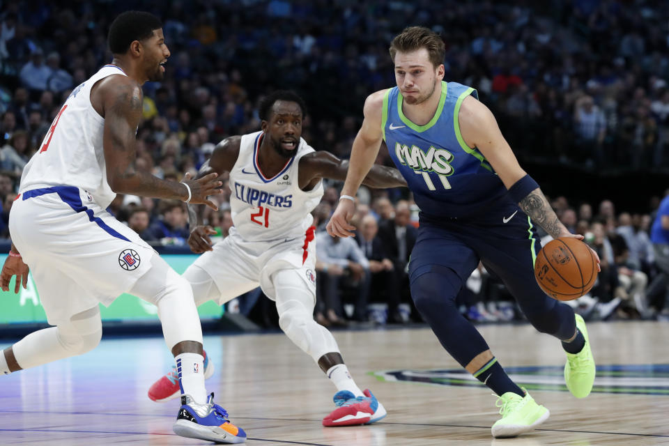 Los Angeles Clippers forward Paul George, left, and Patrick Beverley (21) defend as Dallas Mavericks forward Luka Doncic (77) drives to the basket in the first half of an NBA basketball game in Dallas, Tuesday, Nov. 26, 2019. (AP Photo/Tony Gutierrez)