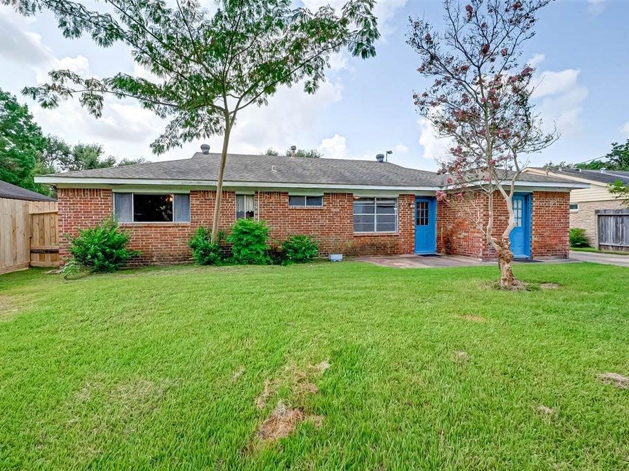 The backyard of a house for sale in houston with grass and blue doors