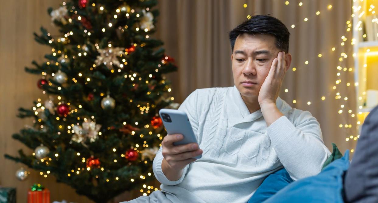 Gambling addiction Christmas man on phone in front of tree. (Getty Images)