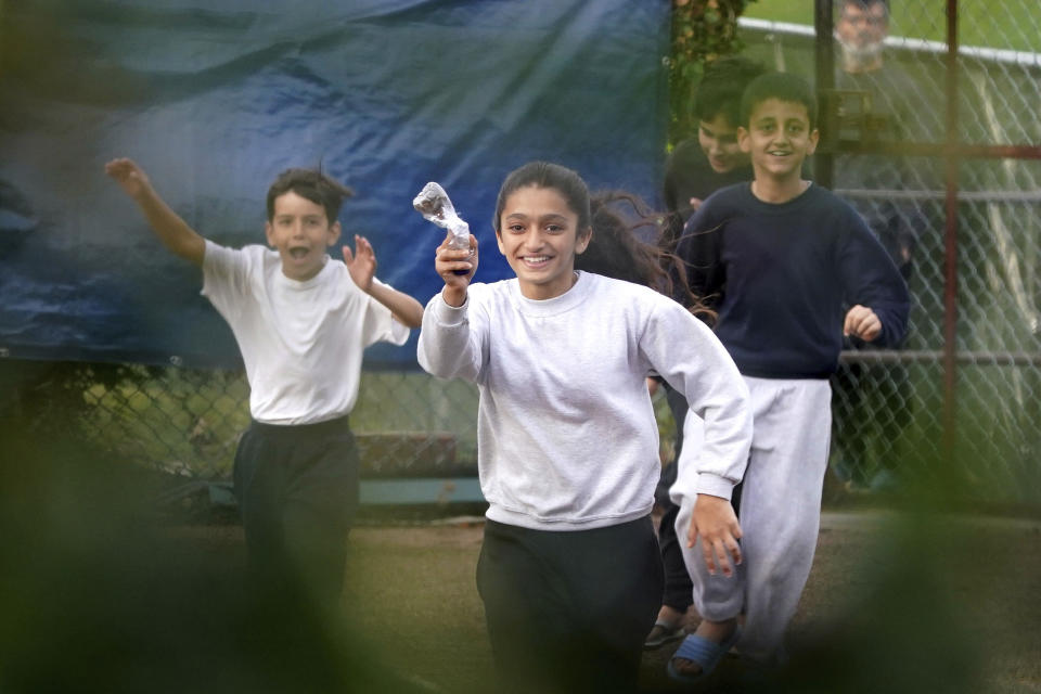 A young girl runs towards the fence carrying a message in a bottle inside the Manston immigration short-term holding facility located at the former Defence Fire Training and Development Centre in Thanet, England, Wednesday, Nov. 2, 2022. Details about overcrowding and inhumane conditions at a migrant processing center in southeast England have shocked Britain and reignited a heated debate about how the Conservative government is handling a sharp increase in the number of asylum-seekers arriving on U.K. shores. (Gareth Fuller/PA via AP)