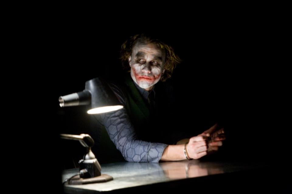 The Dark Knight - 

Medium shot of Heath Ledger as Joker seated at table, wearing handcuffs