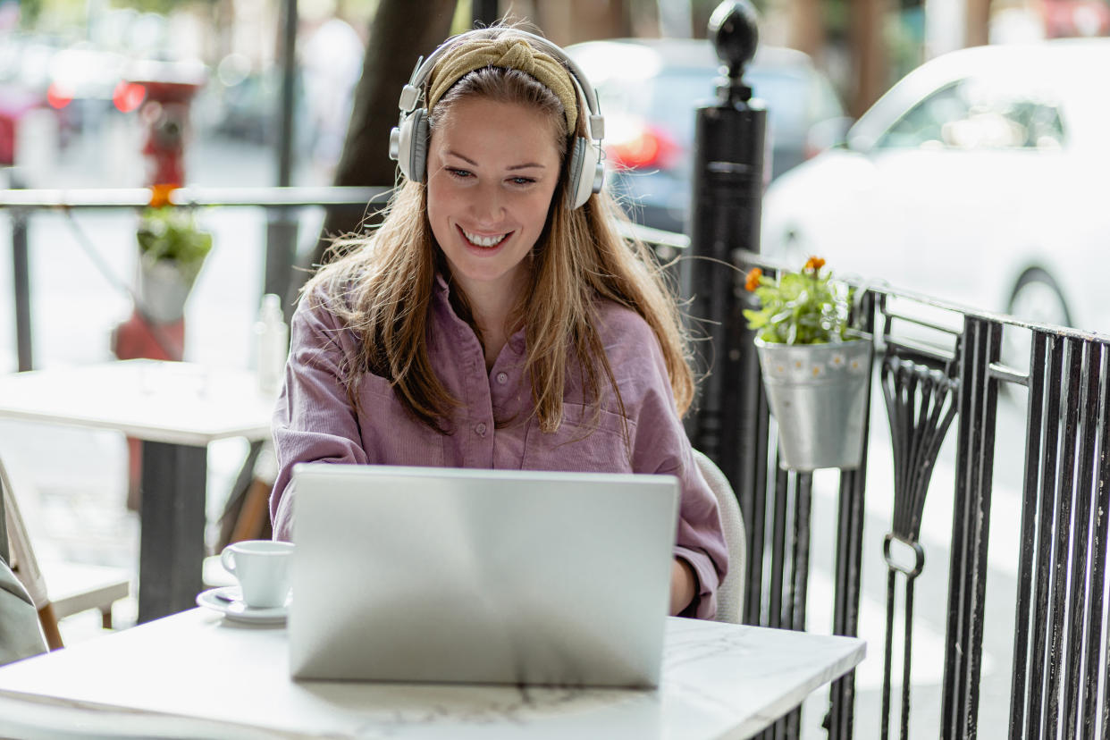 A young woman uses a laptop outdoors and smiling