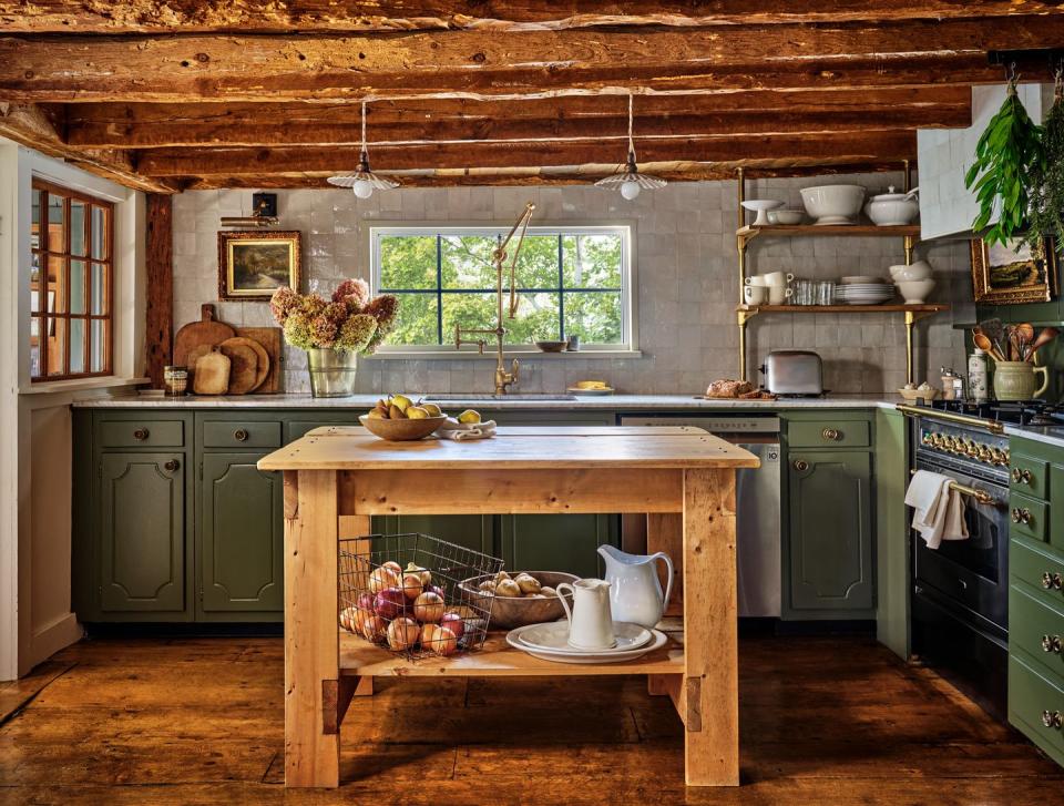 a kitchen with green lower cabinets and low wooden ceiling beams and a wood island in the middle