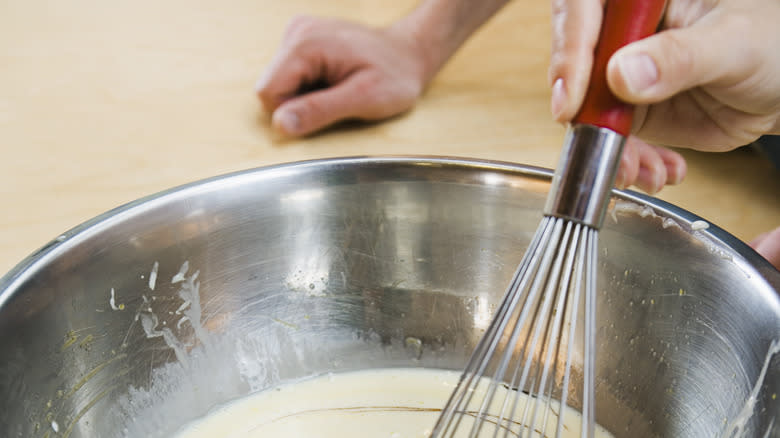 person whisking batter in metal bowl