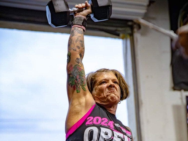 A tattooed woman lifting a barbell at a CrossFit tournament.
