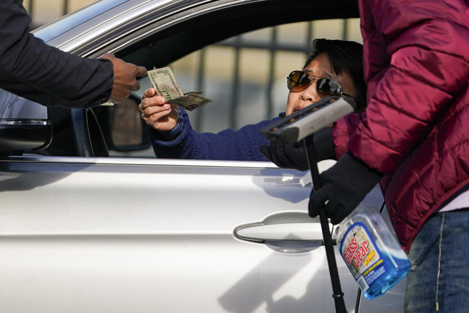 Titi Sangma, center, hands cash to Shamonte Jones, right, and another squeegee worker who offered to clean Sangma's windshields in exchange for cash, Tuesday, Jan. 10, 2023, in Baltimore. "I see him every day," Sangma said about Jones. "He does a good job." Local officials are rolling out their latest plan to steer squeegee workers away from busy downtown intersections and toward formal employment using law enforcement action and outreach efforts. (AP Photo/Julio Cortez)