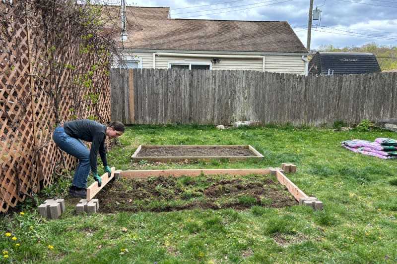 Someone placing wooden planks into planter wall block to make raised bed.