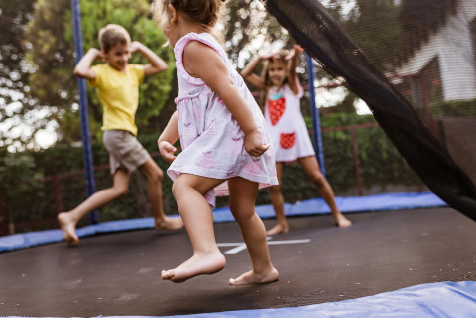 Three children playing and jumping on a trampoline in a backyard