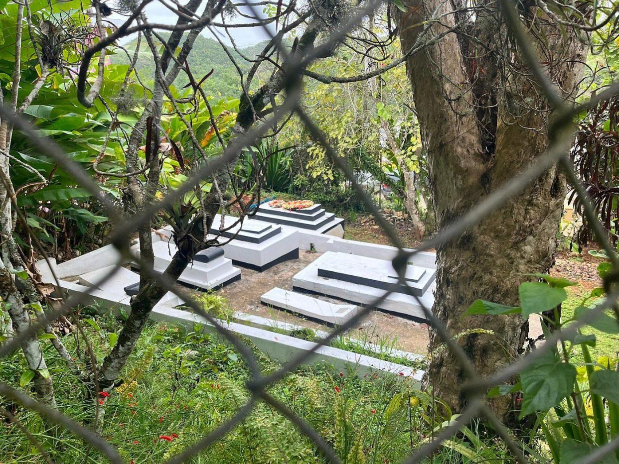 Bob Marley's tomb in the Bob Marley Museum, Nine Mile, Jamaica surrounded by tropical plants and hills in the distance, as seen through a fence