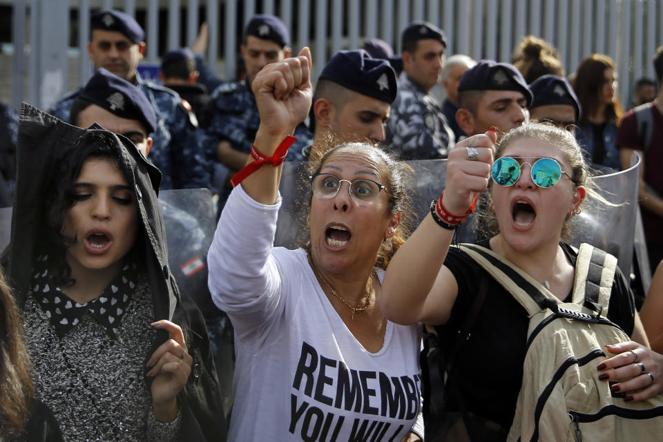 Protesters chant slogans during ongoing protests against the Lebanese political class as riot police stand guard in front of Finance Ministry building in Beirut, Lebanon, Friday, Nov. 29, 2019. Protesters have been holding demonstrations since Oct. 17 demanding an end to widespread corruption and mismanagement by the political class that has ruled the country for three decades. (AP Photo/Bilal Hussein)