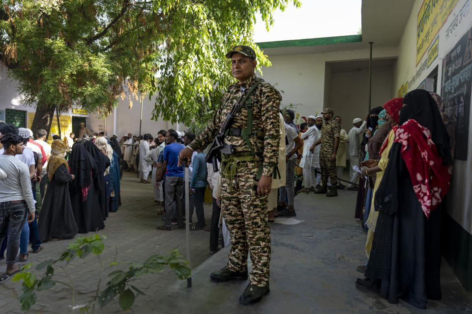 A security personnel stands guard as people queue up to vote during the second round of voting in the six-week-long national election in Nahal village near Meerut, in Uttar Pradesh, India, Friday, April 26, 2024. (AP Photo/Altaf Qadri)