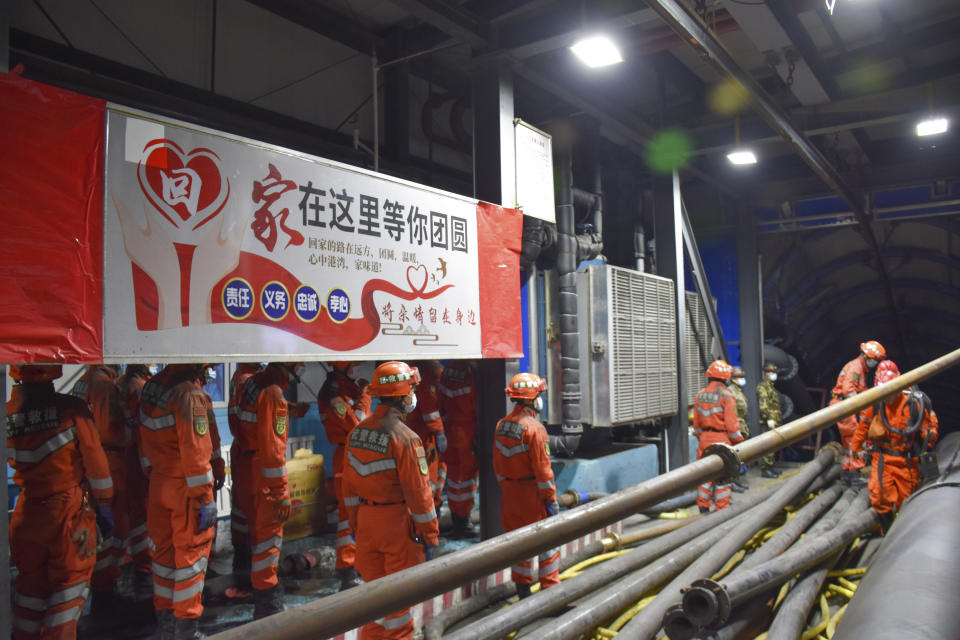 In this photo released by Xinhua News Agency, rescue workers stand near a banner which reads: "Home is waiting for your region" at the entrance to a flooded coal mine in Hutubi county in of Hui Autonomous Prefecture of Changji, northwest China's Xinjiang Uyghur Autonomous Region on Sunday, April 11, 2021. Some miners were reported trapped after the coal mine flooded on Saturday. (Gao Han/Xinhua via AP)