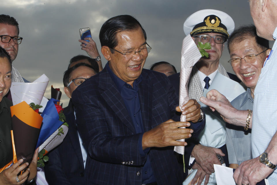 Cambodia's Prime Minister Hun Sen, center, gives a flower to a passenger who disembarked from the MS Westerdam, owned by Holland America Line, at the port of Sihanoukville, Cambodia, Friday, Feb. 14, 2020. Hundreds of cruise ship passengers long stranded at sea by virus fears cheered as they finally disembarked Friday and were welcomed to Cambodia. (AP Photo/Heng Sinith)