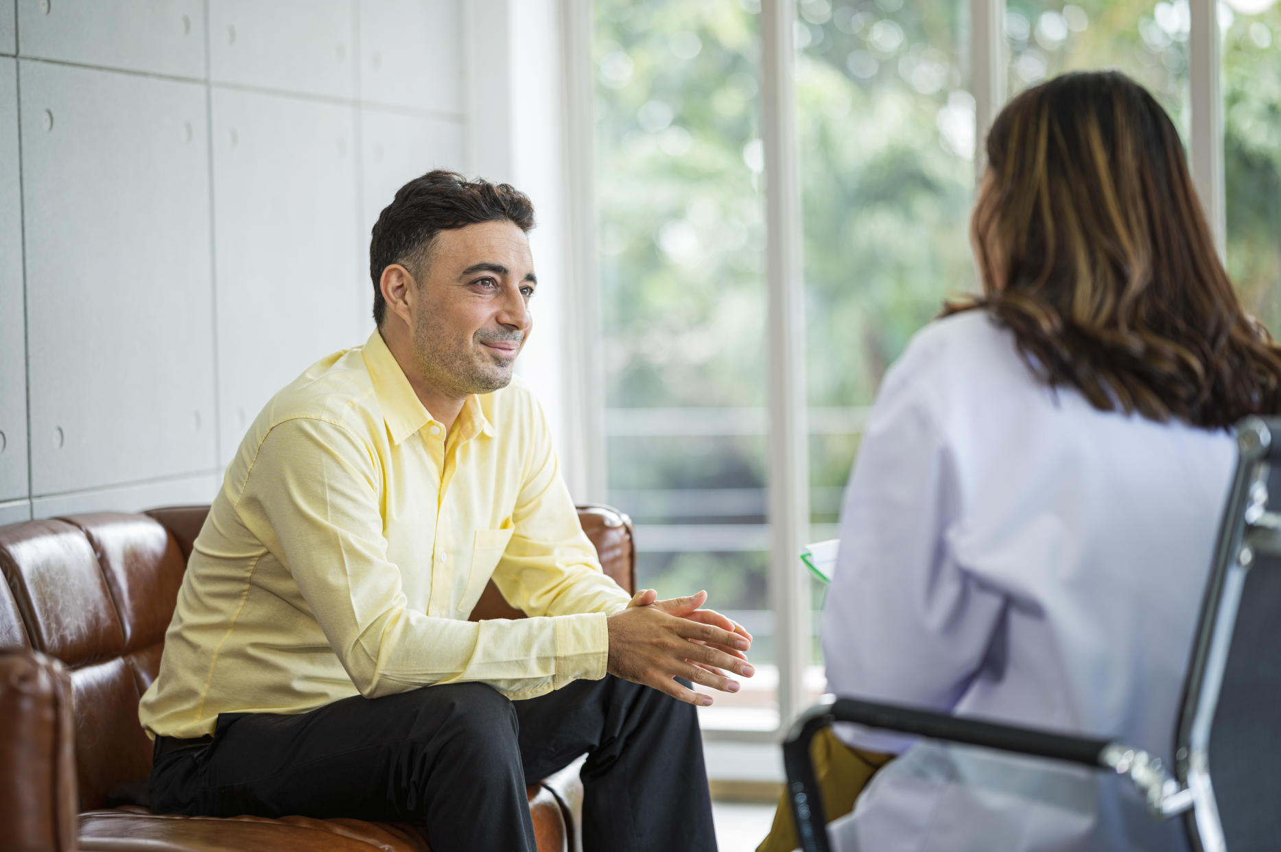 A Senior Man sits on a sofa with his therapist , discuss and gestures as his speaks to her. Hopeful expression, Mental health and counseling concept.