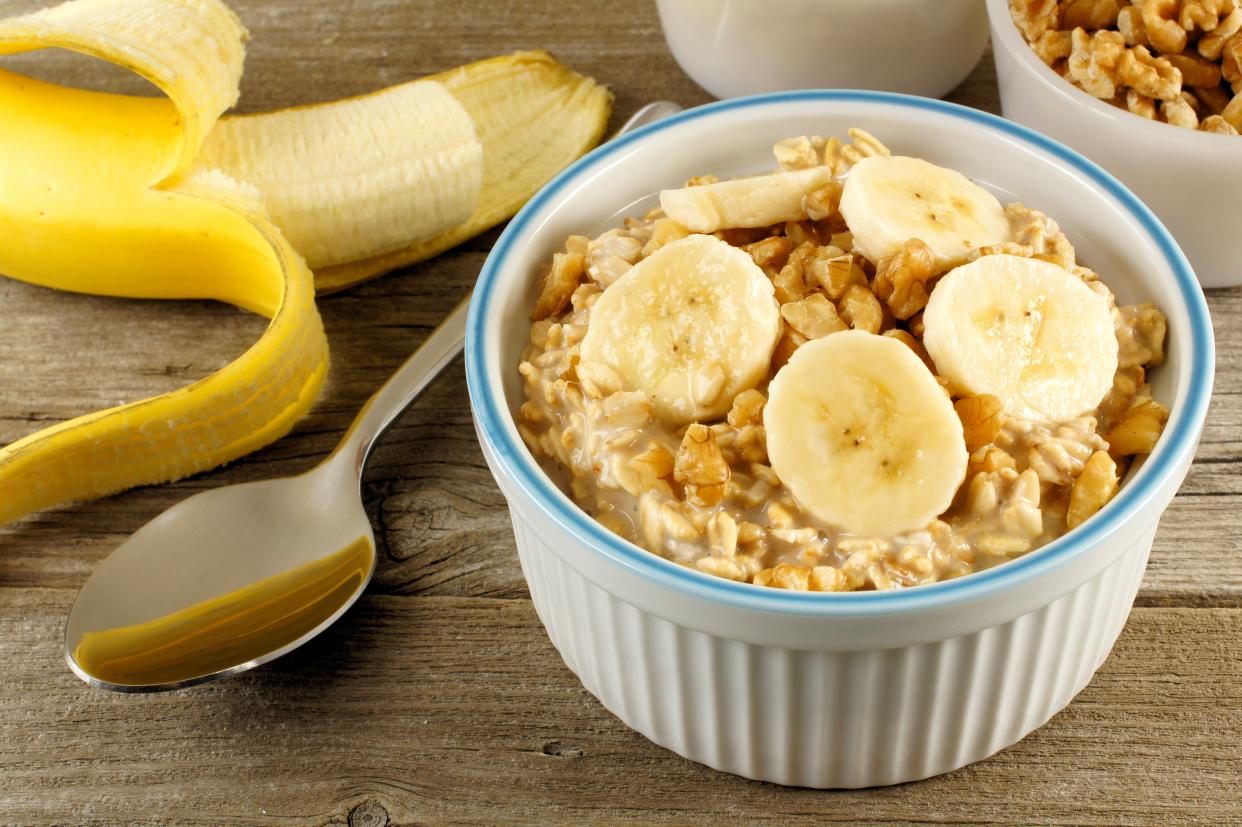 Oatmeal with banana slices and nuts in a white container on a wood table