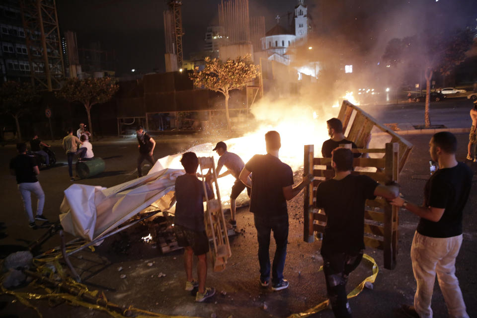 An anti-government protester sets fire to plastic barriers and trash to block a road during a demonstration in Beirut, Lebanon, Thursday, Oct. 17, 2019. Scores of people are protesting in Beirut and other parts of Lebanon over the government's plans to impose new taxes amid a harsh economic crisis in the country. (AP Photo/Hassan Ammar)