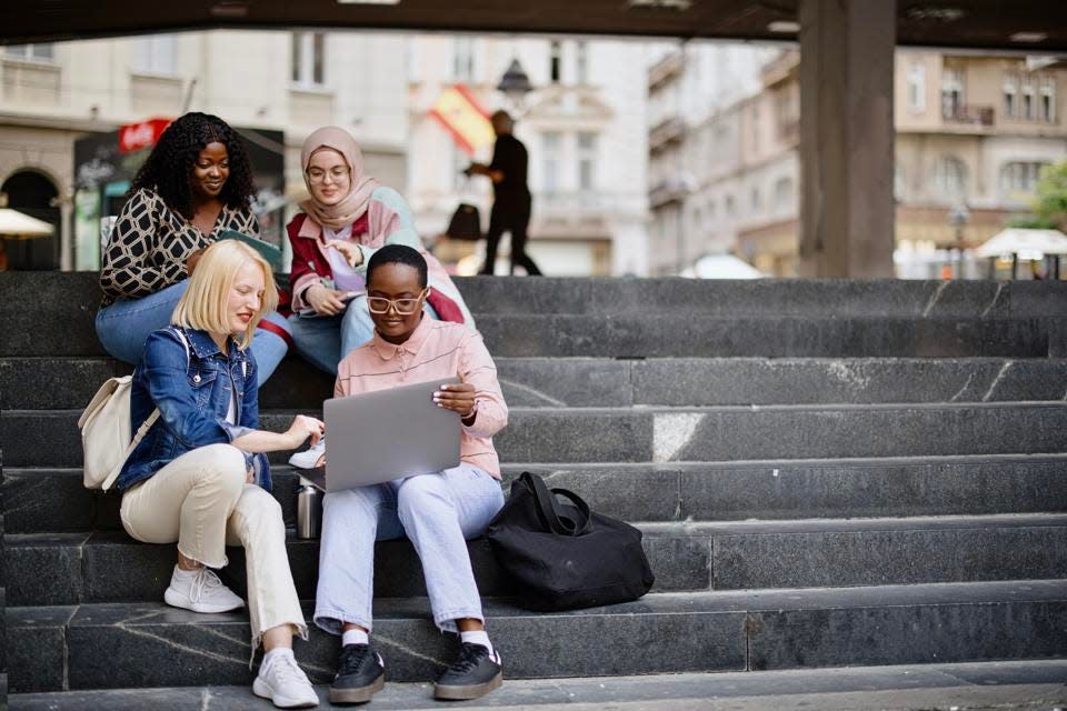 Los estudiantes se sientan en los escalones cerca de la universidad y miran la computadora portátil.