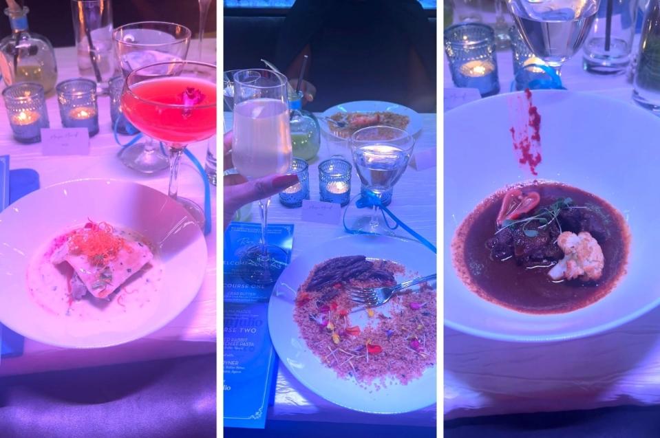 Three dishes on a table illuminated by blue light, with a person's hand holding a cocktail