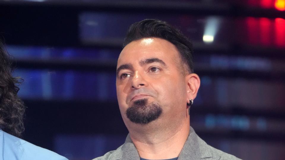 chris kirkpatrick standing with his arms cross at his waist and holding a microphone