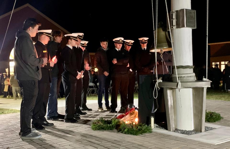 A group of Maine Maritime Academy students gather around a memorial set up on the Castine, Maine campus on Sunday, Dec. 11, 2022, to remember four students who died in a fiery weekend SUV crash just off campus.