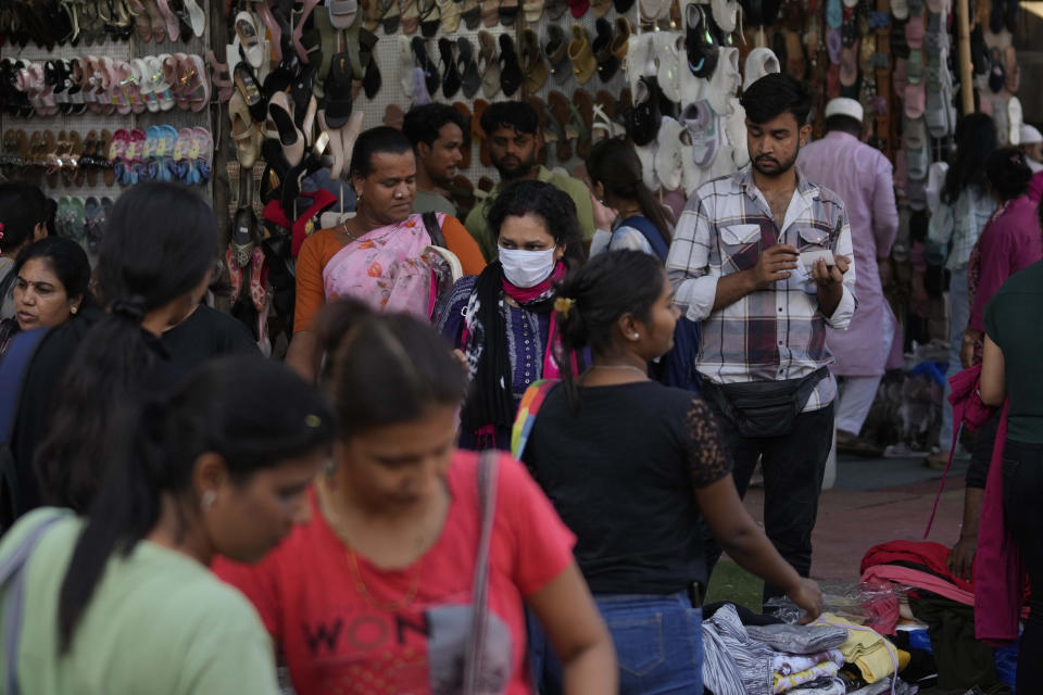 A woman wearing a face mask walks through a busy shopping district in Mumbai, India, Thursday, Dec. 22, 2022. India has begun randomly testing international passengers arriving at its airports for COVID-19, the country’s health minister said Thursday, citing an increase in cases in neighboring China and also asked the public to wear masks and maintain social distancing. (AP Photo/Rafiq Maqbool)