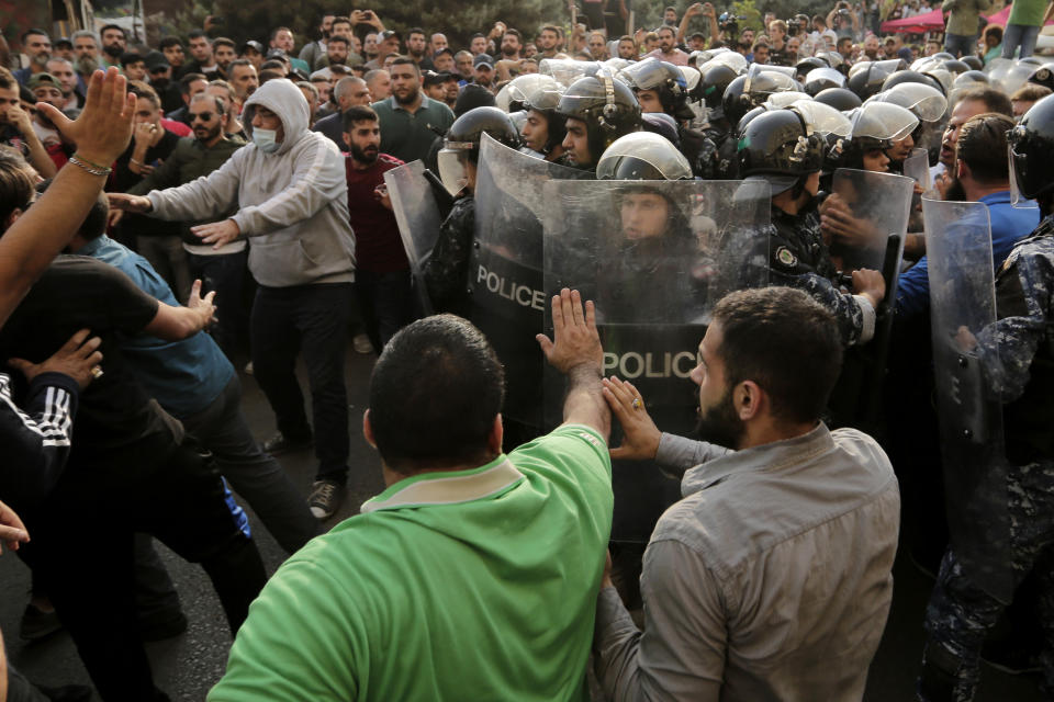 Lebanese riot policemen stand guard between anti-government protesters, background, and Hezbollah supporters after they clash between each other during a protest in Beirut, Lebanon, Friday, Oct. 25, 2019. Leader of Lebanon's Hezbollah calls on his supporters to leave the protests to avoid friction and seek dialogue instead. (AP Photo/Hassan Ammar)