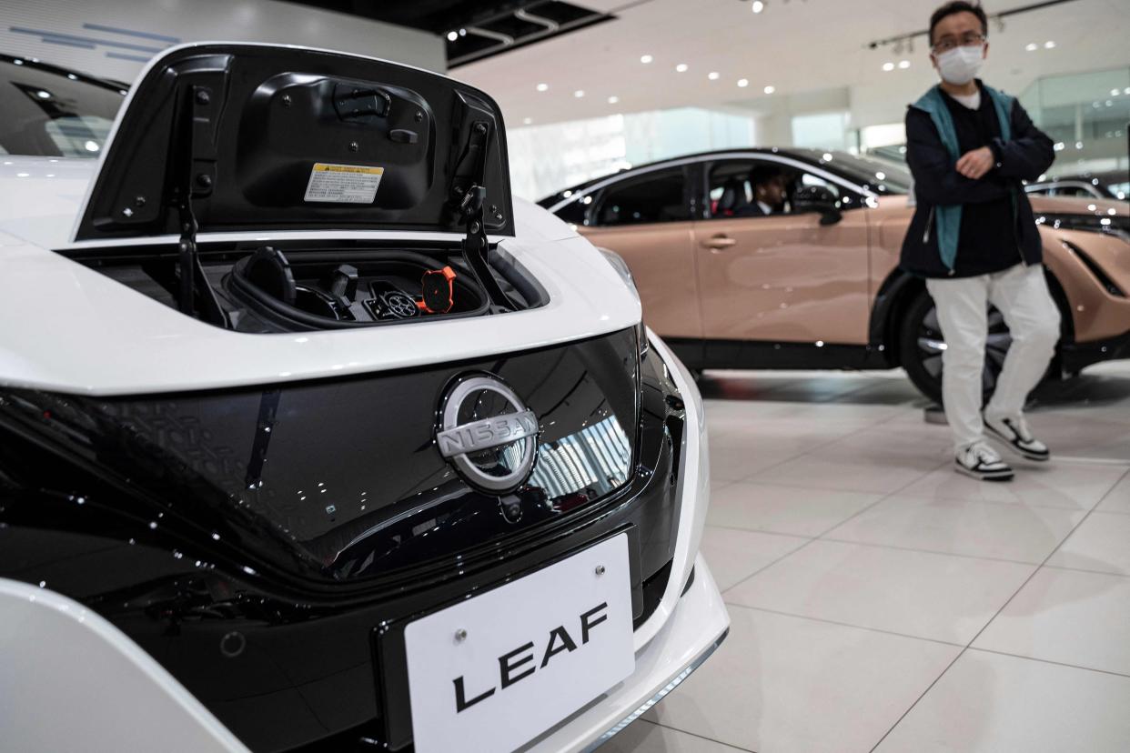This photo taken on March 30, 2023 shows a man walking past one of Nissan's electric vehicles (EV), the Leaf, at the global headquarters of Japanese automaker Nissan Motor in Yokohama, Kanagawa prefecture.