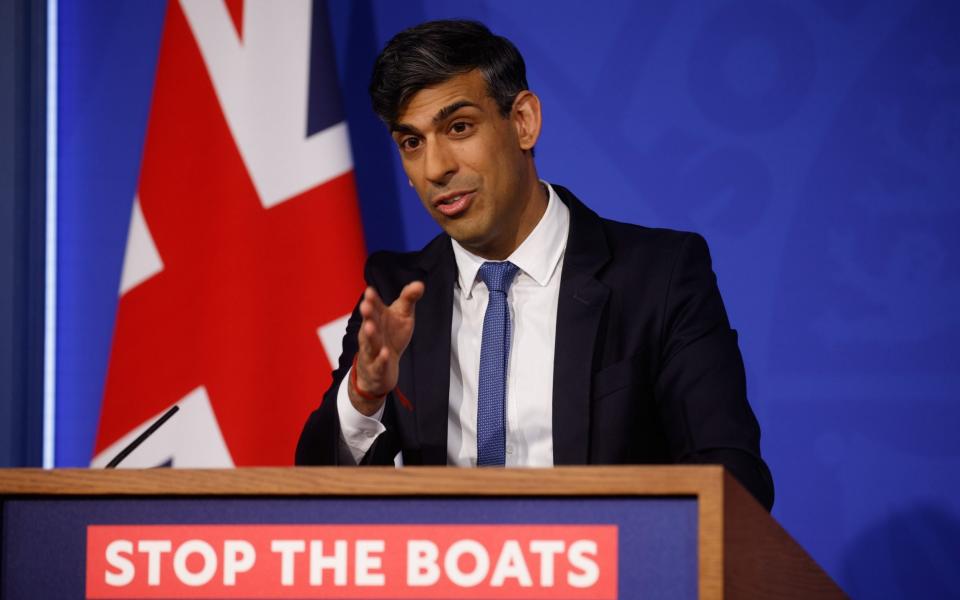 Rishi Sunak gestures behind a lectern marked 'STOP THE BOATS'